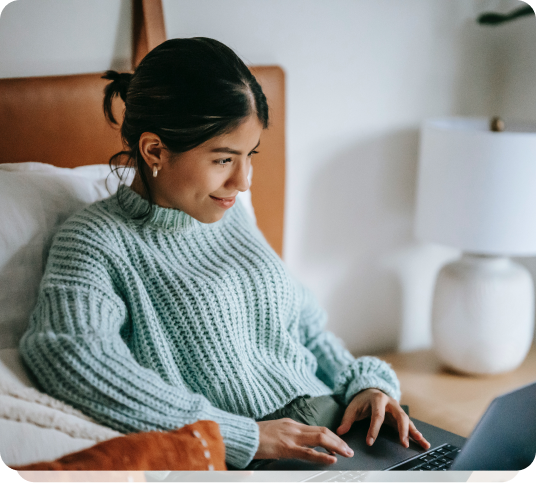 a woman sitting on a bed using a laptop computer